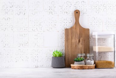 Mutfak tezgahının üstünde kavanozlar ve beyaz arka planda kesim tahtaları var.