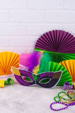 Mardi Gras arka planında mor, altın ve yeşil süslemeler, boncuklar ve karnaval maskesi var.