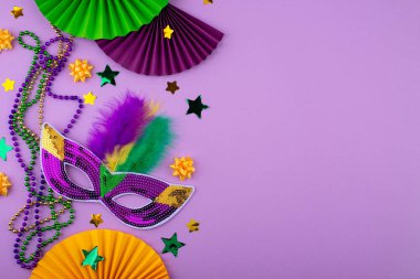 Mardi Gras arka planında mor, altın ve yeşil süslemeler, boncuklar ve karnaval maskesi var.