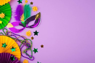 Mardi Gras arka planında mor, altın ve yeşil süslemeler, boncuklar ve karnaval maskesi var.