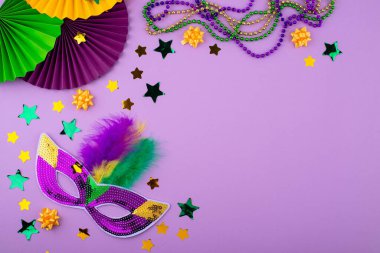 Mardi Gras arka planında mor, altın ve yeşil süslemeler, boncuklar ve karnaval maskesi var.