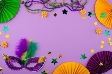 Mardi Gras arka planında mor, altın ve yeşil süslemeler, boncuklar ve karnaval maskesi var.