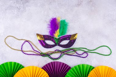Mardi Gras arka planında mor, altın ve yeşil süslemeler, boncuklar ve karnaval maskesi var.