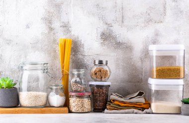 Mutfak tezgahının üstünde kavanozlar ve beyaz arka planda kesim tahtaları var.