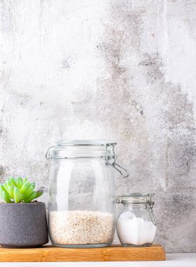 Mutfak tezgahının üstünde kavanozlar ve beyaz arka planda kesim tahtaları var.