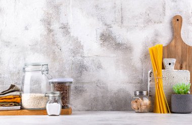 Mutfak tezgahının üstünde kavanozlar ve beyaz arka planda kesim tahtaları var.