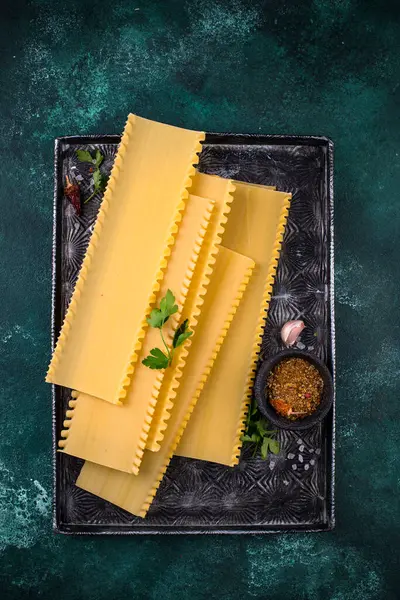 Pişmemiş çiğ lazanya makarna ve yeşil arka planda pişirme malzemeleri.