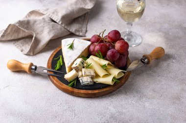 Bir bardak şarap, değişik türde yumuşak peynir ve üzümler.