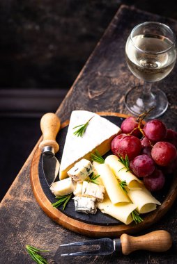 Bir bardak şarap, değişik türde yumuşak peynir ve üzümler.