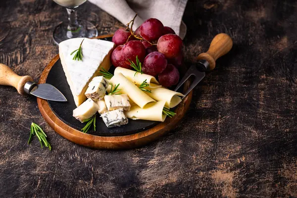 Bir bardak şarap, değişik türde yumuşak peynir ve üzümler.