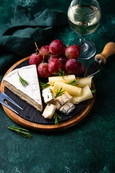 Bir bardak şarap, değişik türde yumuşak peynir ve üzümler.