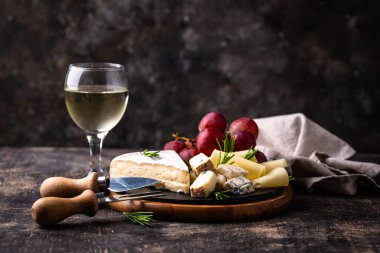 Bir bardak şarap, değişik türde yumuşak peynir ve üzümler.