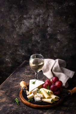 Bir bardak şarap, değişik türde yumuşak peynir ve üzümler.