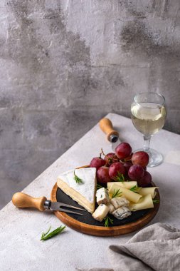 Bir bardak şarap, değişik türde yumuşak peynir ve üzümler.