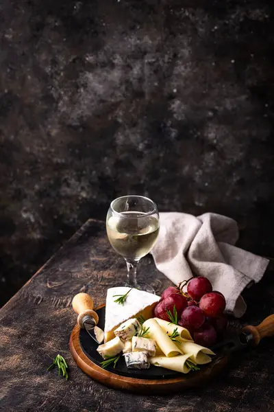 Bir bardak şarap, değişik türde yumuşak peynir ve üzümler.