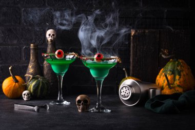 Balkabaklarıyla ve kafataslarıyla çevrili yeşil kokteyller koyu arka planda.