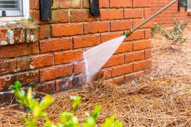 Pressure washer using water to clean a dirty brick wall on a house. clipart