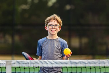 Pickleball teçhizatı olan genç çocuk sahada.