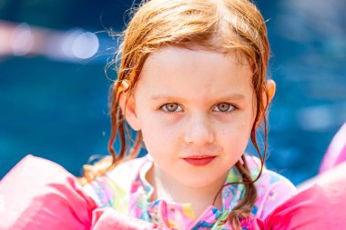 Genç kız yüzme havuzunda oynarken kameraya bakıyor..