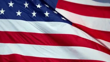Mavi gökyüzüne karşı canlı kırmızı beyaz ve mavi renklerle rüzgarda dalgalanan gerçek Amerikan bayrağının uzun görüntüleri..