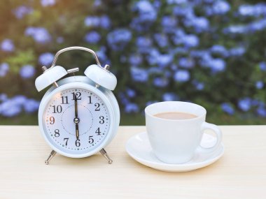 Mor çiçekli bahçedeki masada beyaz antika çalar saat ve bir fincan kahve..