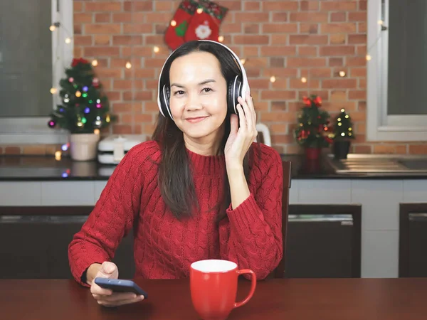 스웨터를 아시아 크리스마스 장식을 부엌에 커피가 식탁에 헤드폰을 핸드폰에서 음악을 — 스톡 사진