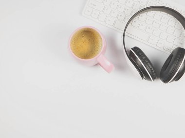 Bilgisayar klavyesinde düz kulaklık ve beyaz arka planda pembe kahve..