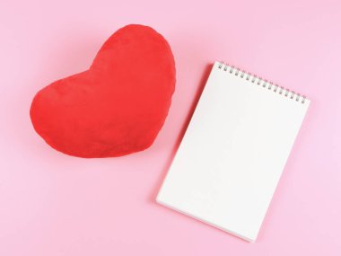 Top view or flat lay of opened  notebook with red heart shape pillow  on pink background with copy space. Love, Valentine's day, memory.