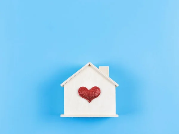 Top view or flat lay of wooden model house with red glitter heart on blue background. dream house , home of love, strong relationship, valentines.