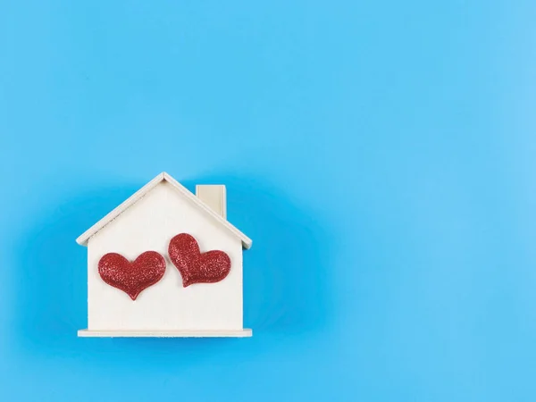 Top view or flat lay of wooden model house with two red glitter hearts on blue background. dream house , home of love, strong relationship, valentines.