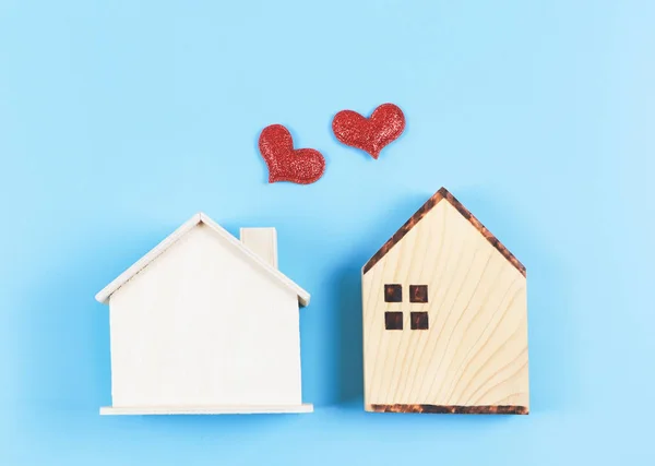 Top view or flat lay of two wooden model houses with red glitter hearts on blue background. dream house , home of love, strong relationship, neighboring houses, valentines.