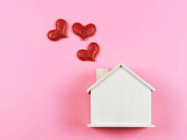 Top view or flat lay of wooden model house with red glitter hearts on pink  background. dream house , home of love, strong relationship, valentines.