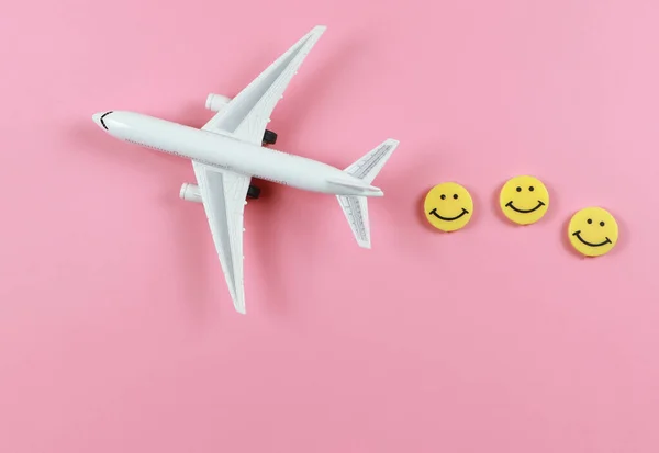 Top view or flat lay of airplane model with three yellow circle smiling faces  on pink  background. Happy or fun trip concept.