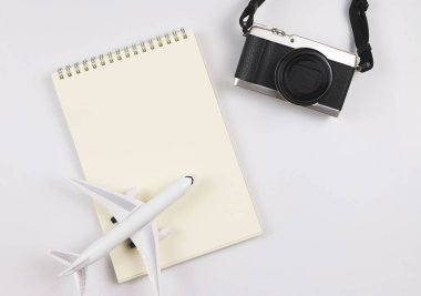 Top view or flat lay of blank page opened notebook, airplane model  and camera on white  background with copy space. Travel, photo and memory concept.