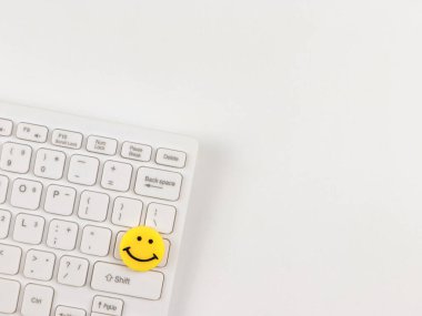 Top view or flat lay of  yellow circle smiling face on white computer keyboard on white  background.