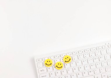 Top view or flat lay of  three yellow circle smiling faces on white computer keyboard on white  background.