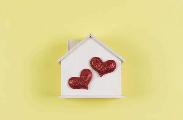 Top view or flat lay of wooden model house with two red glitter hearts on yellow  background. dream house , home of love, strong relationship, valentines.