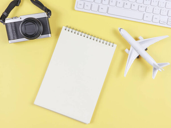 Top view or flat lay of airplane model, computer keyboard, opened blank page notebook and digital camera with copy space on yellow background, business and traveling concept.