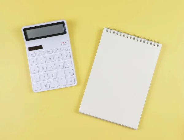 stock image Top view or flat lay of white calculator with blank page opened notebook on yellow background. business and education concept.