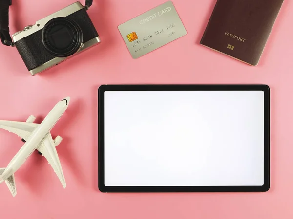 Top view or flat lay of digital tablet with blank white screen, airplane model, passport, credit card and digital camera isolated on pink background. travel planning concept.