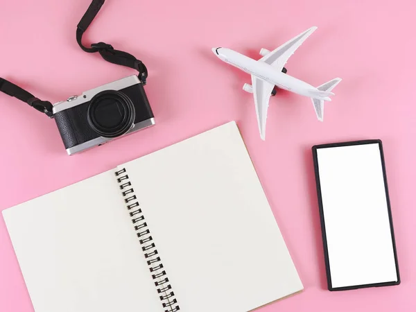 stock image Top view or flat lay of blank paper note book, blank white screen mobile phone,  airplane model  and camera on pink background. Travel plan concept.