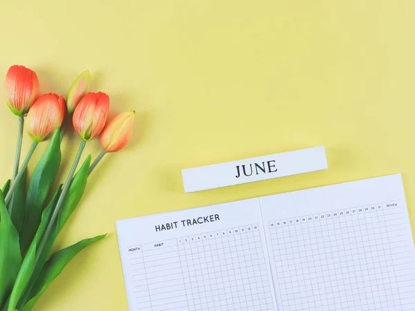 Top view or flat lay of habit tracker book with wooden calendar June,   and tulips  on yellow background.