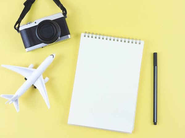 Top view or flat lay of blank page opened notebook with pen, airplane model and digital camera on yellow background with copy space.