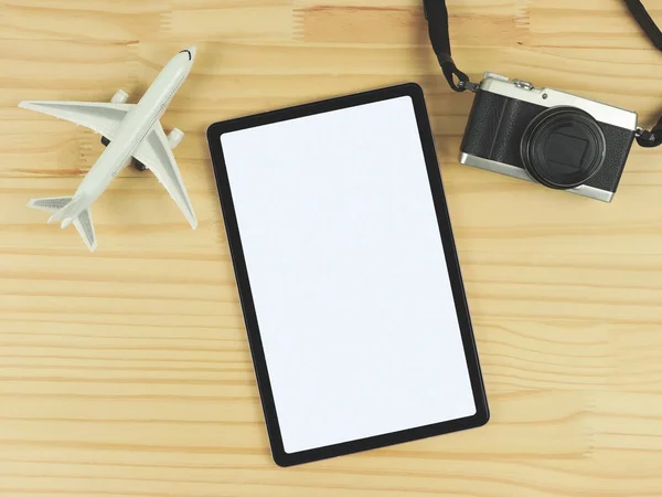 Top view or flat lay of digital tablet with blank white screen, airplane model and digital camera isolated on wooden table  background. travel planning concept.