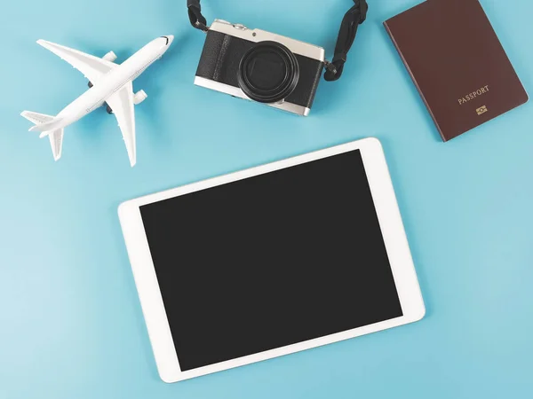 Top view or flat lay of digital tablet with blank black screen, airplane model, passport and digital camera isolated on blue background. travel planning concept.