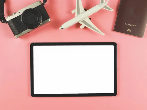 Top view or flat lay of digital tablet with blank white screen, airplane model, passport and digital camera isolated on pink background. travel planning concept.