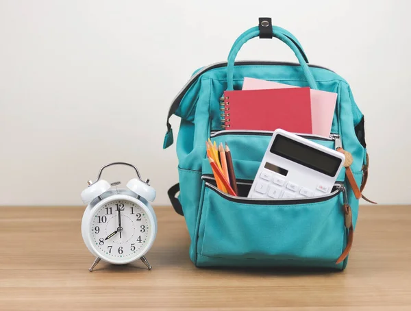 stock image Back to school concept.Front view  of green backpack with school supplie and white vintage alarm clock 8 o'clock on wooden table and white  background with copy space.