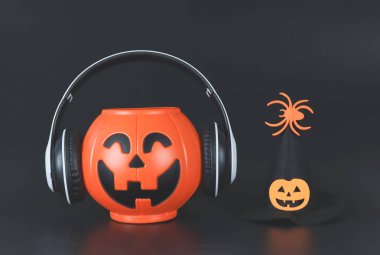 Kulaklıkla kaplı plastik cadılar bayramı balkabağı örtüsü ve balkabağı yüzüyle süslenmiş cadılar bayramı şapkası ve siyah arka planda izole edilmiş örümcek..