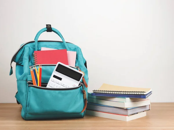 Back to school concept.Front view of green backpack with school supplie, stack of books on wooden table and white  background with copy space.