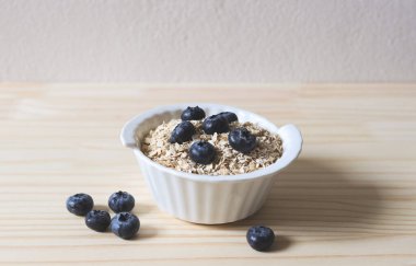 Kahvaltının önü yulaflı ya da beyaz kasede granola, ahşap masada taze yaban mersini. Sağlıklı kahvaltı kavramı.